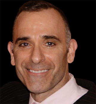 A man in a suit and tie smiles for the camera in a marketing photoshoot.