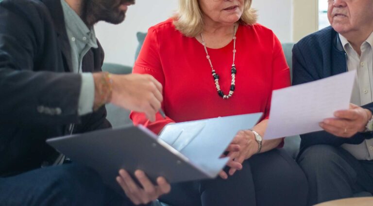 Three older people sitting around a table looking at papers discussing digital marketing strategies for business growth online.