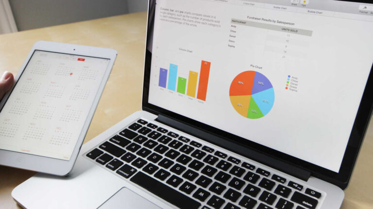 A person is holding a laptop and a tablet while analyzing graphs to help businesses grow online with SEO assistance.